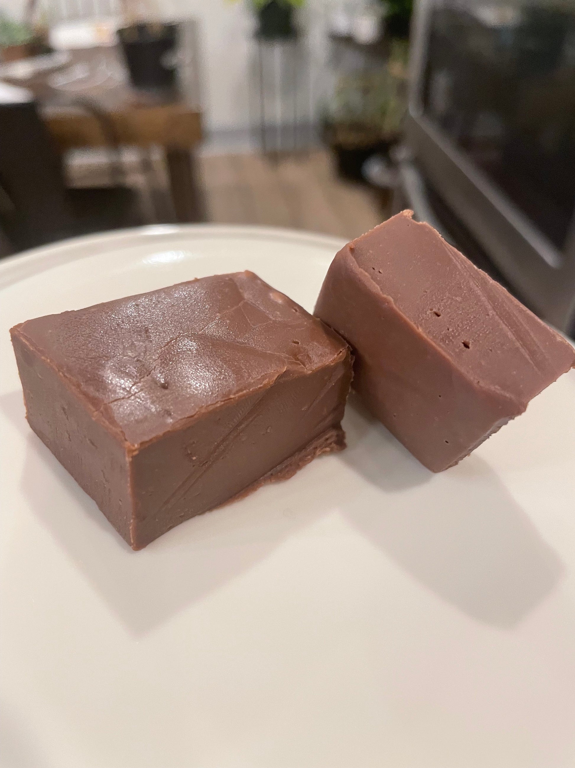 Two pieces of chocolate fudge on a white surface with a blurred background
